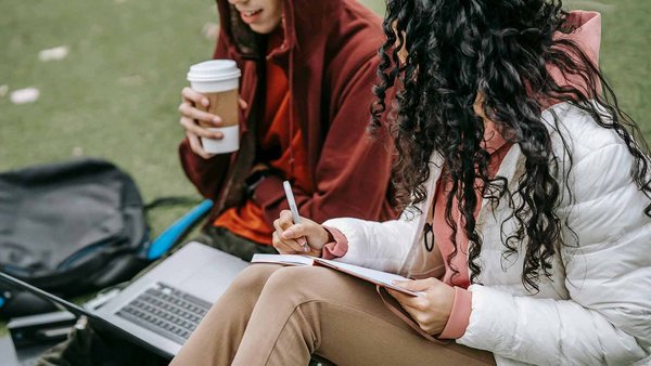 Zwei Studierende sitzen auf einer Wiese und lernen zusammen